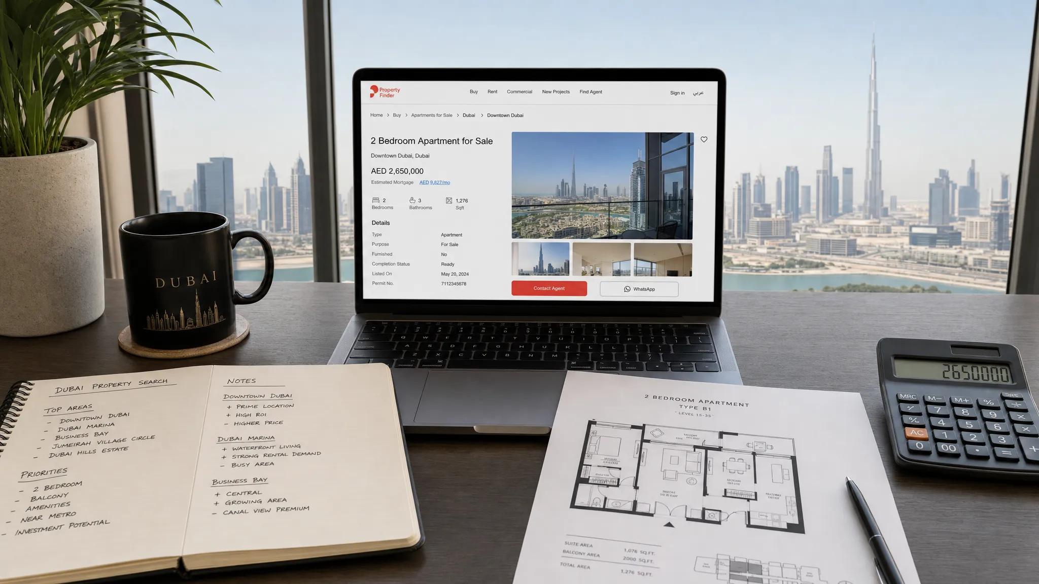 A Dubai property search workspace with neighborhood notes, a printed floor plan, a calculator, and a laptop showing a property listing page with the screen facing forward and unobstructed, arranged on a desk beside a window with a city view.