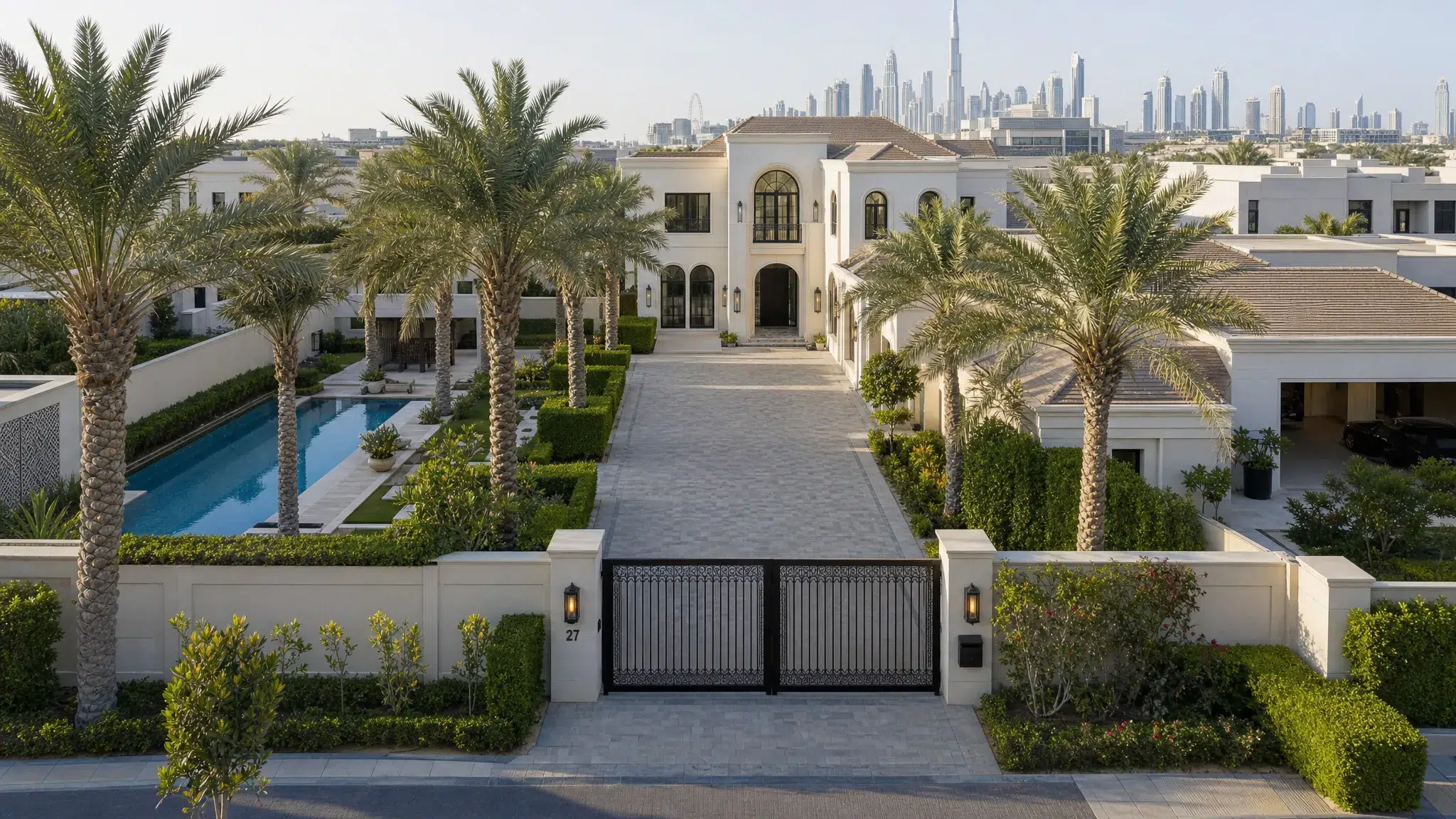 A private modern mansion in Dubai with a long driveway, landscaped gardens, tall palm trees, a swimming pool, and a quiet gated entrance in an upscale residential community, shown from a slightly elevated front angle.